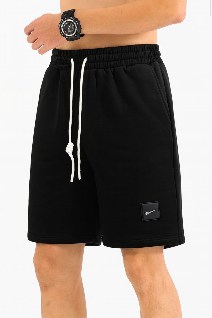 Black Nike athletic shorts with white drawstrings and a small black Nike logo patch on the lower left leg, shown on a model against a white background.