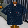 A short-sleeve button-up shirt by Levi's in navy blue with a small white geometric pattern, displayed on a wooden hanger on a mannequin stand in a living room setting.