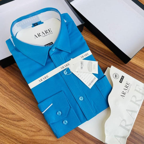 A folded bright blue long-sleeve dress shirt with ARARE branding, displayed on a wooden surface with its packaging tags and boxes.