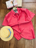 A coral pink short-sleeve button-up shirt laid flat on a wooden floor, styled with a yellow straw hat featuring a blue and white striped band and two product boxes at the top.