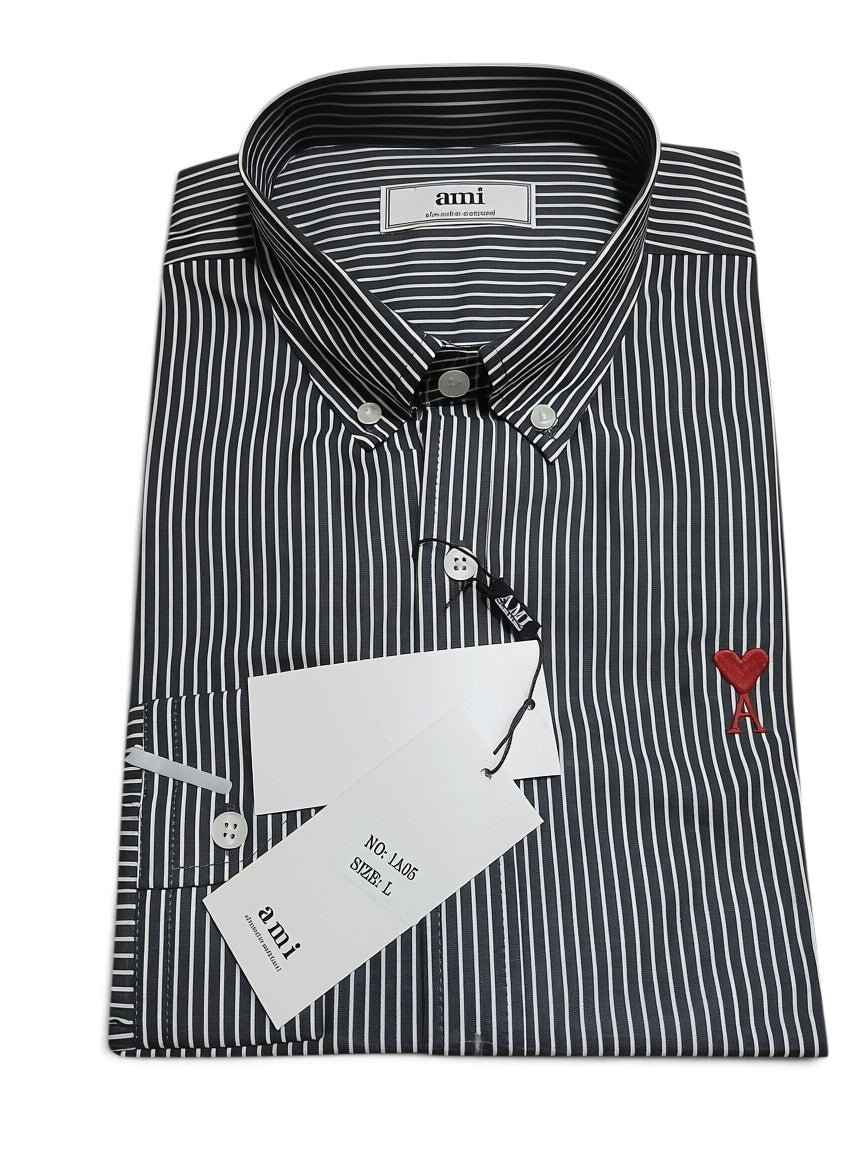 A folded Ami brand long-sleeve button-down shirt with thin vertical gray and white stripes, featuring a small red embroidered logo on the chest and a white hangtag.