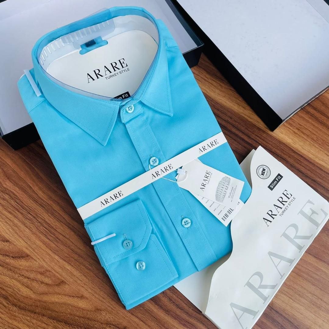 A folded light blue long-sleeve dress shirt with ARARE branding, displayed on a wooden surface with its packaging box and care card.