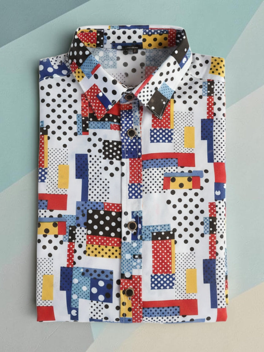 A long-sleeve button-down shirt with a vibrant, multicolored geometric patchwork print featuring blocks of red, blue, yellow, black, and white with polka dots, laid flat on a light blue and gray geometric background.
