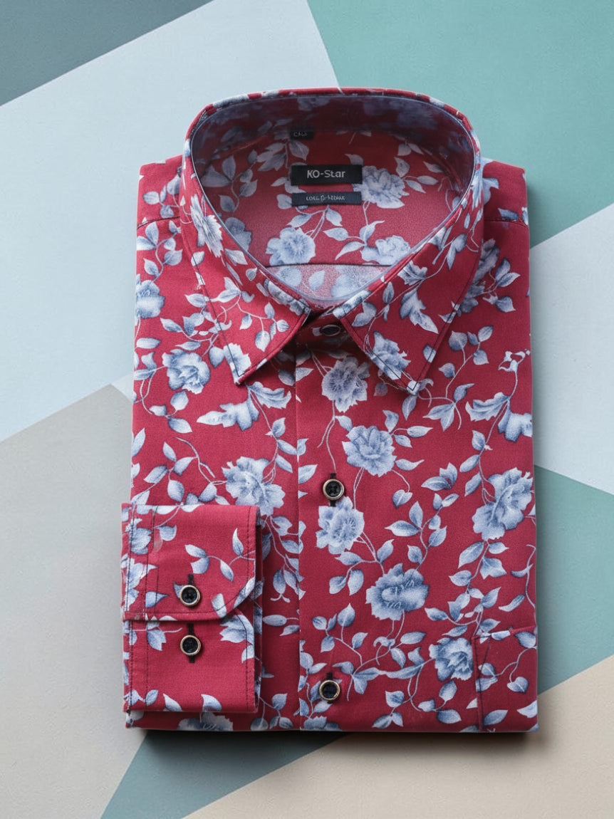 A folded red dress shirt with a blue and white floral pattern, featuring a button-down front and a single-button cuff, laid flat on a geometric background.