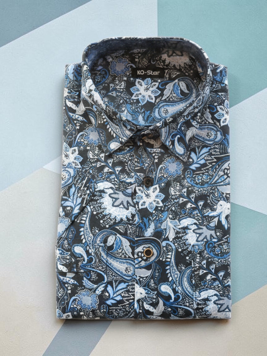 A folded long-sleeve button-up shirt with a detailed blue, white, and black paisley and floral pattern, displayed on a geometric background.