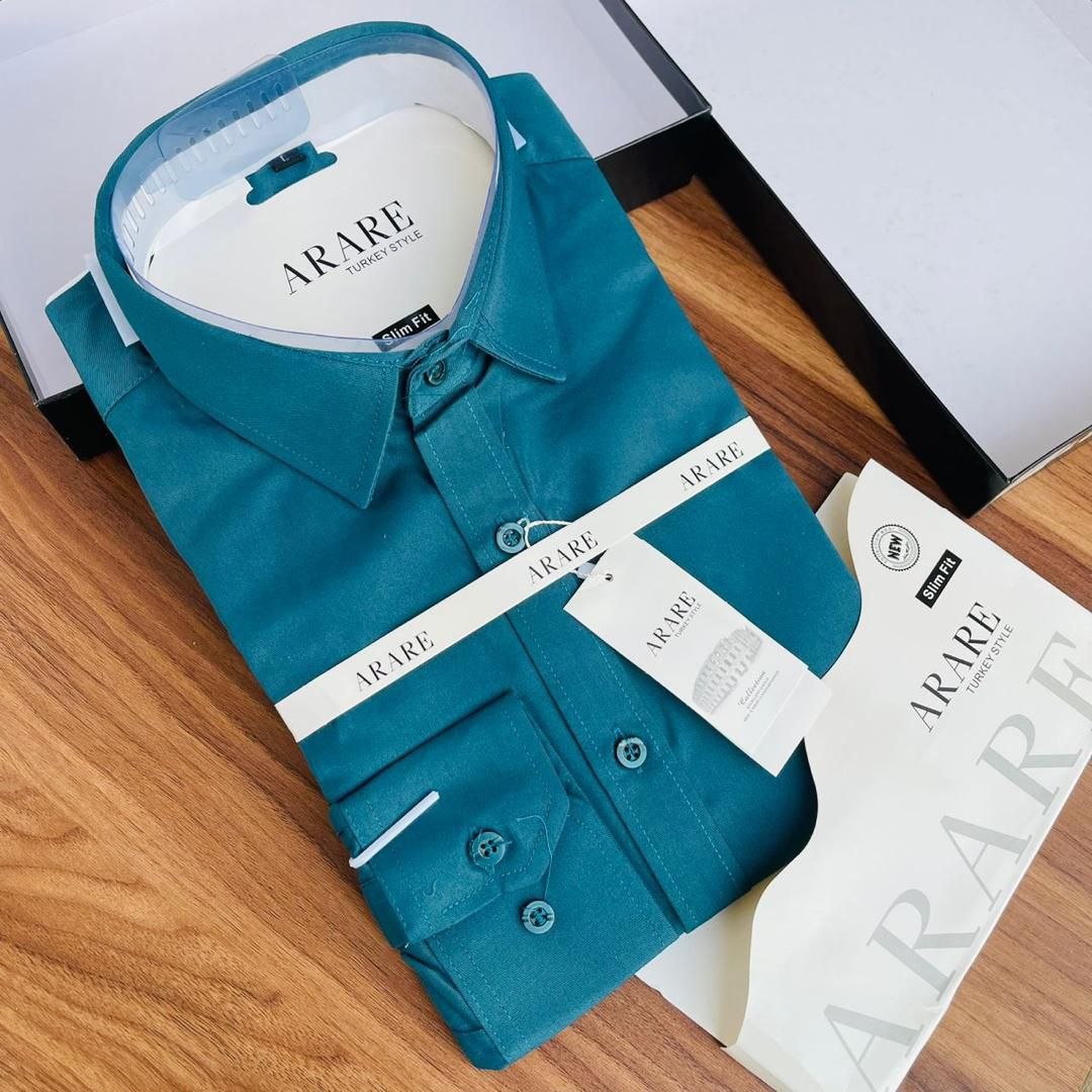 A folded teal blue long-sleeve dress shirt with ARARE branding, displayed on a wooden surface next to its packaging box and shopping bag.